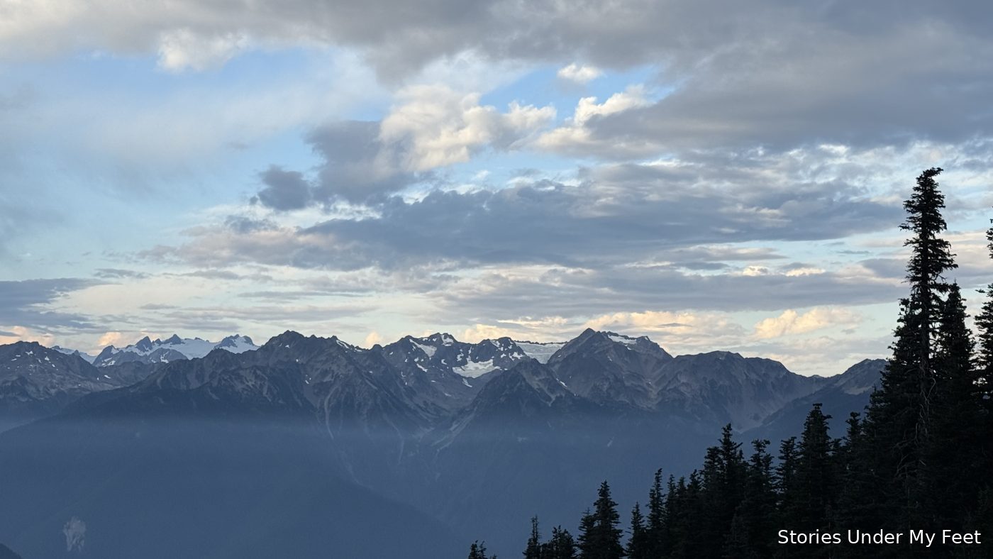 Snow-dusted peaks of the Olympic Mountains under a wide, cloud-streaked sky